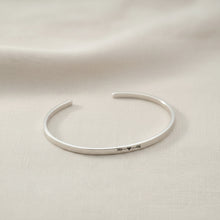 A sterling silver open cuff bracelet with a fletched heart design in the center, 
