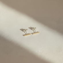 Gold bar earrings on a beige fabric background