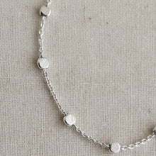 Silver bracelet with small round embellishments on a textured beige background
