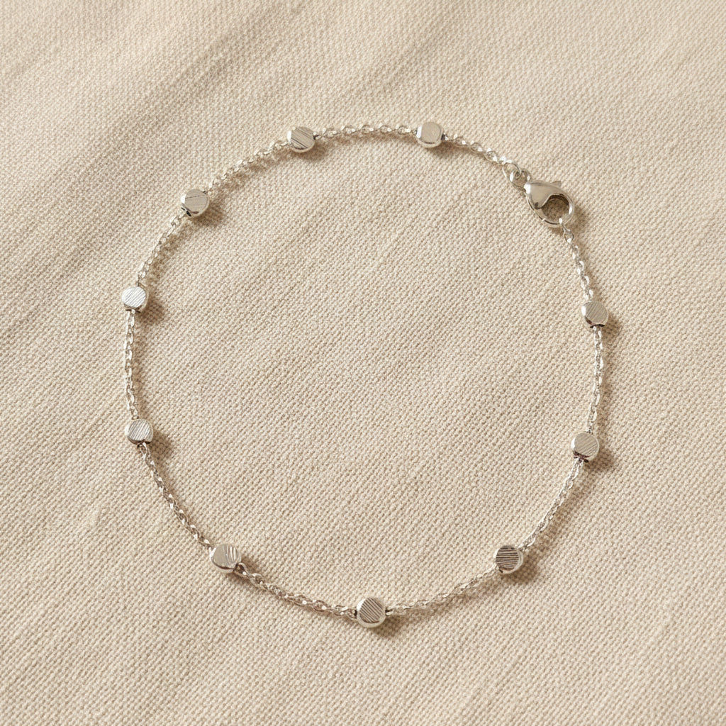 Silver bracelet with disc beads on a beige fabric background