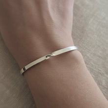 A close-up of a person's wrist wearing a thin polished silver cuff bracelet.