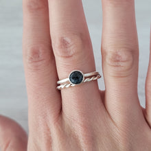 A hand wearing a sterling silver ring with a bezel-set teal kyanite gemstone