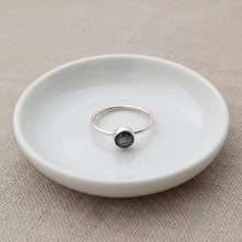 Silver ring with a teal kyanite gemstone on a white ceramic dish against a beige fabric background
